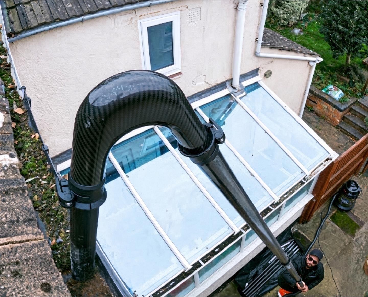 Long-reach vacuum pole clearing gutters over a conservatory from the ground.